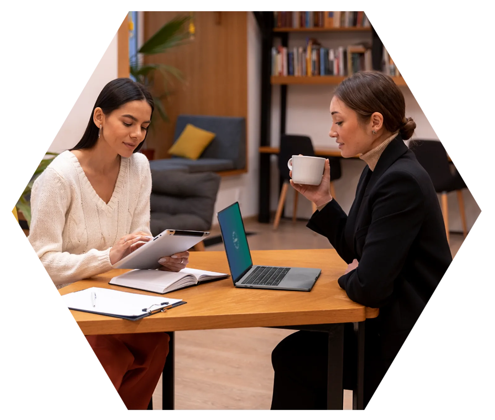 Women Collaborating | CAQA LLND Two women discuss work at a table with a laptop, demonstrating CAQA LLND's focus on employability skills.